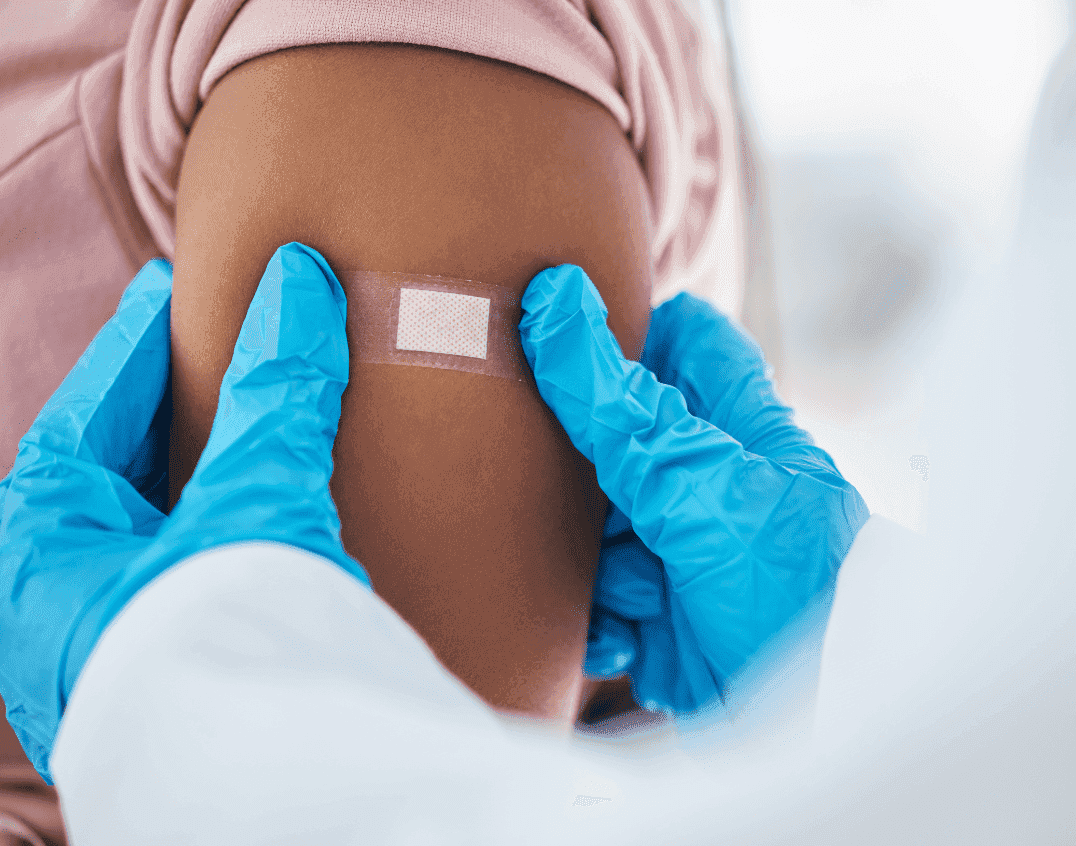 Woman getting band-aid placed on her upper arm by a healthcare professional in blue gloves